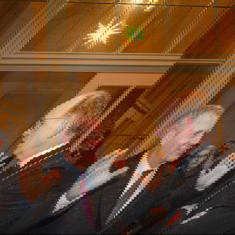 Zwei Männer, einer gestikulierend, stehen vor einer Glastür, hinter der ein gelber Stern leuchtet. 