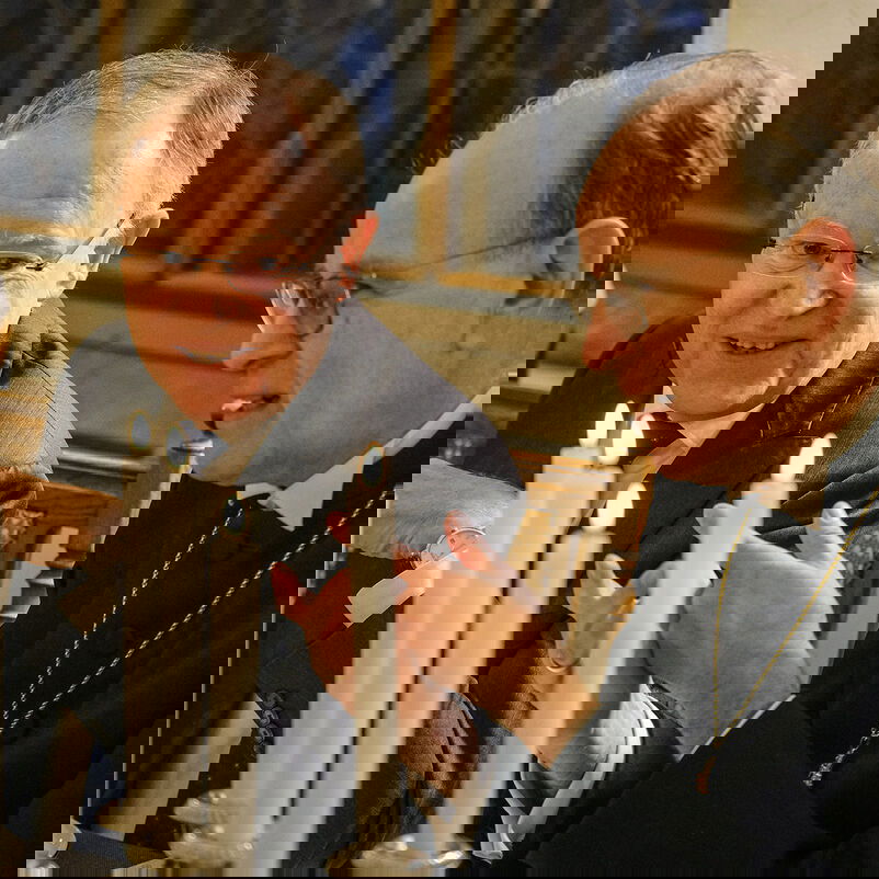 Zwei Männer sitzen nebeneinander und gestikulieren. Vor ihnen ein gedeckter Tisch mit Kerzenleuchtern.