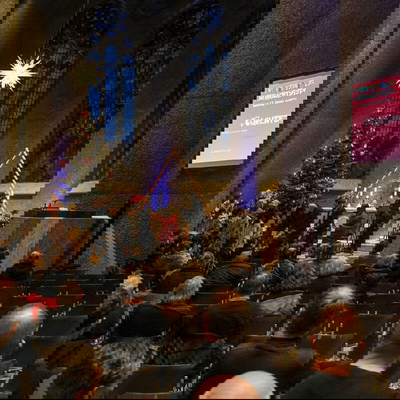 Blick über zwei oder drei dutzend Köpfe hinweg in einen Altarraum in dem ein Stern hell leuchtet und eine Leinwand steht. Auf der steht: Fürchtet Euch nicht.