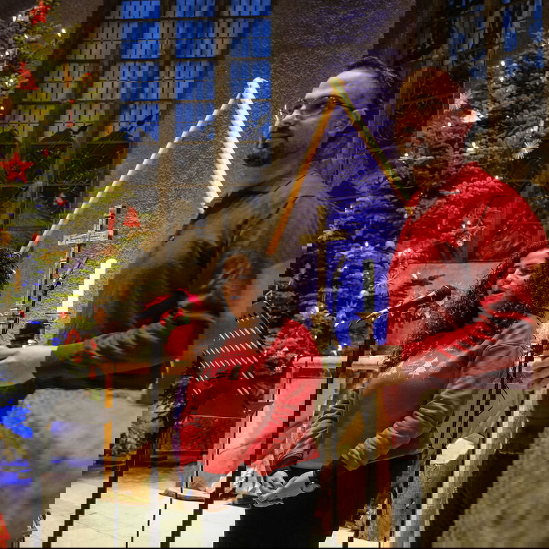 Eine schwarze Frau und ein Mann stehen an Mikrophonen vor einem großen Weihnachtsbaum in einer Kirche.