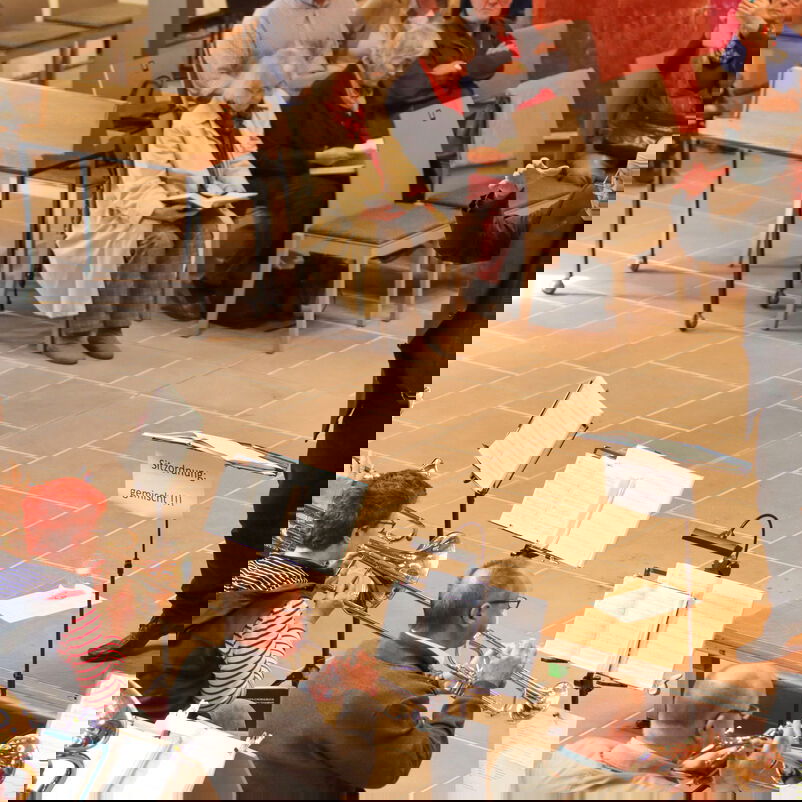 Ein schwarzgekleideter Dirigent steht vor Musizierenden mit Notenständern.