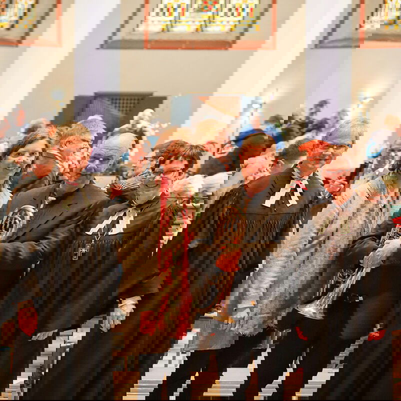 Vier Personen, zwei davon in Talaren, stehen zusammen vor hohen Kirchenfenstern.