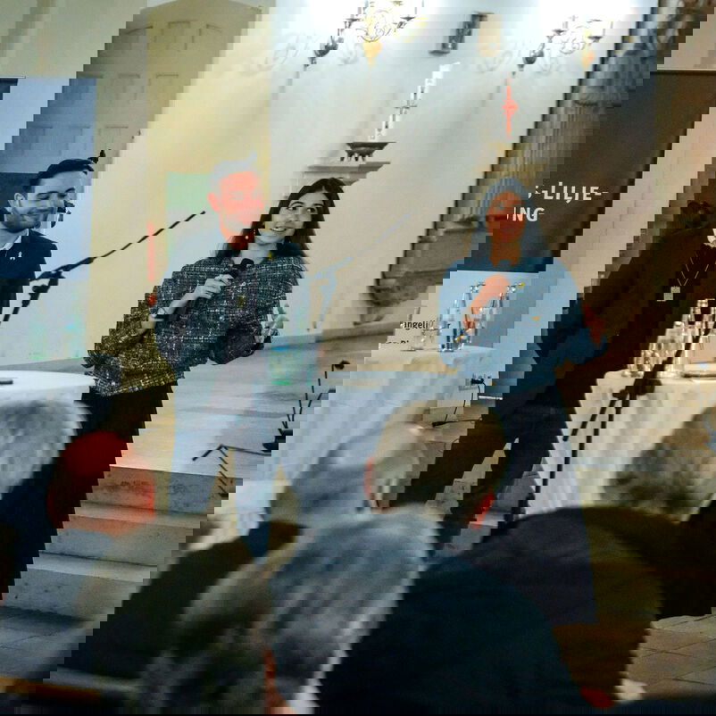 Vier Personen stehen im Halbkreis vor einem Mikro vor weiterem Publikum.