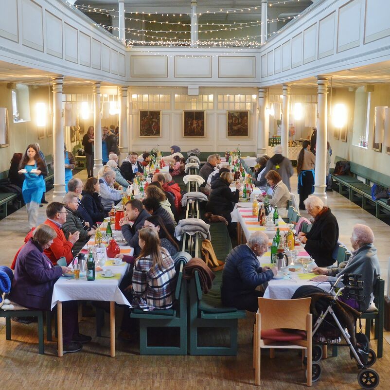 Menschen sitzen an langen Tafeln.