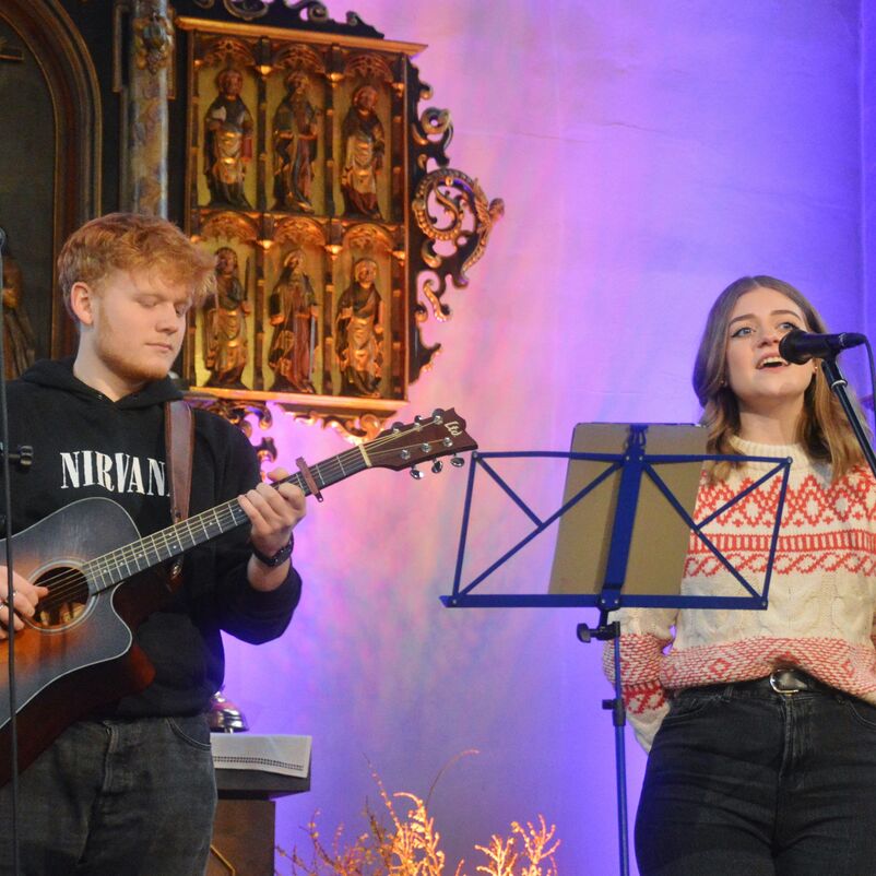Zwei Menschen machen Musik: Einer spielt Gitarre, die andere Person singt.