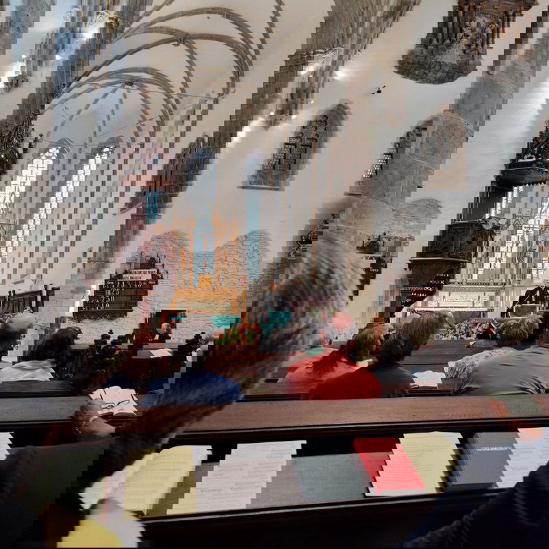 Blick aus einer Bankreihe in einer Kirche auf den Altarraum.