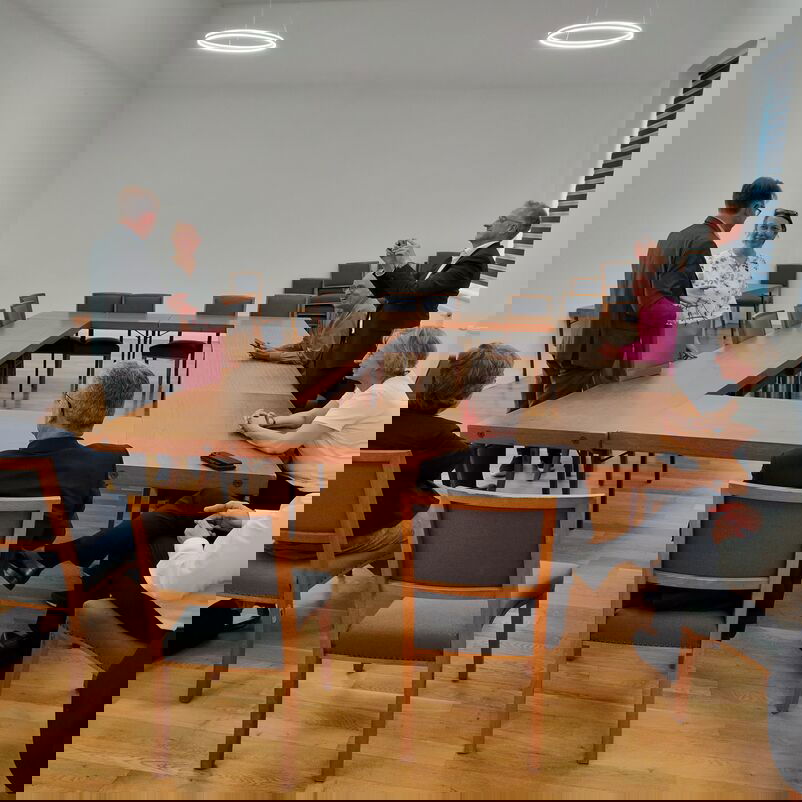 Eine Gruppe von weiblich und männlich zu lesenden Personen sitzt um einen Tisch und diskutiert.