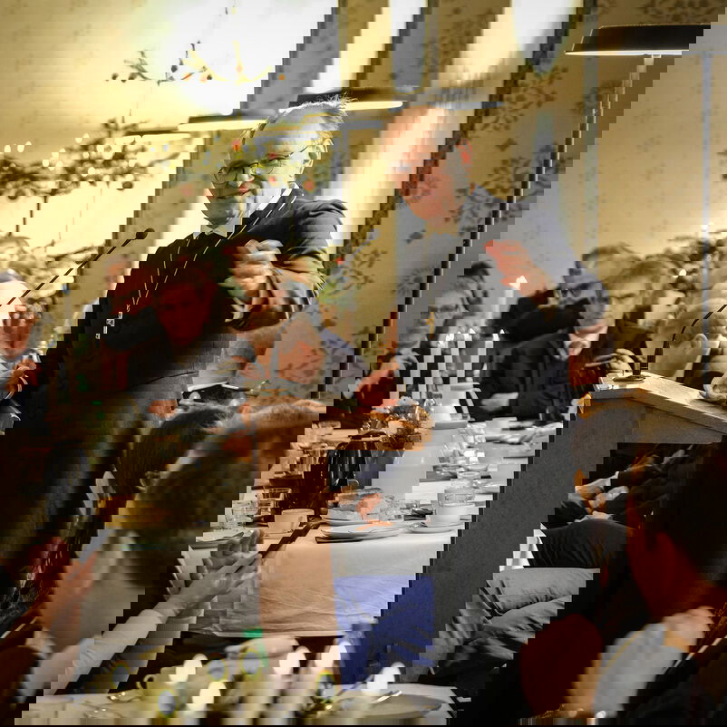 Mehrere Menschen sitzen an gedeckten Tischen, eine Person steht und spricht.