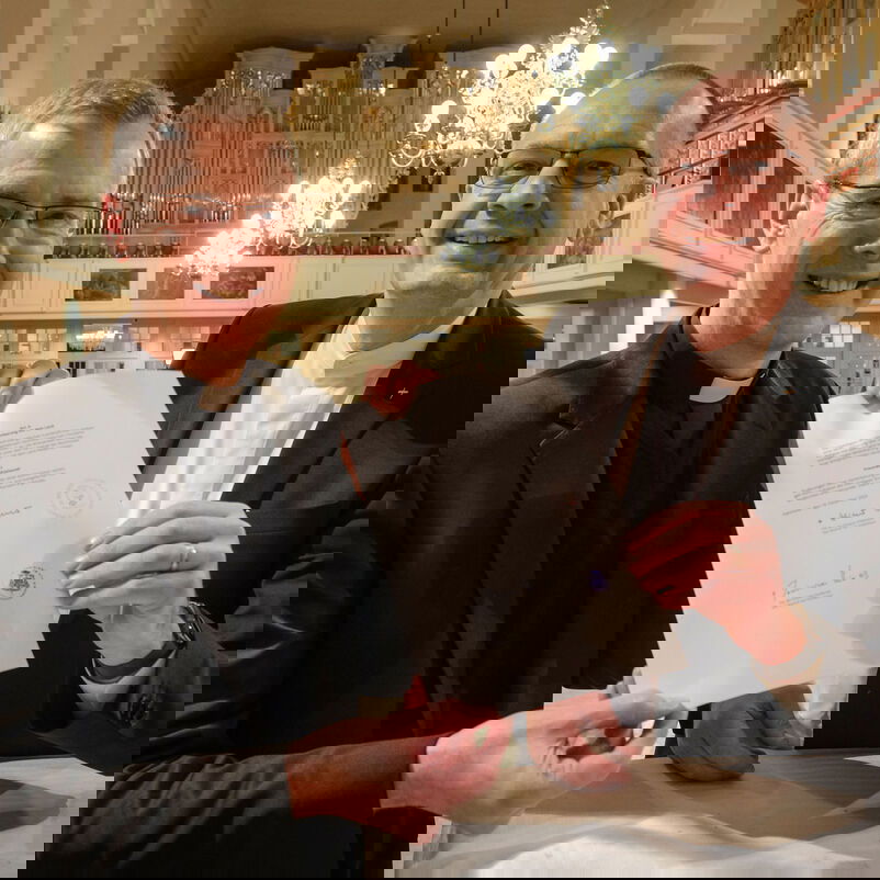 Zwei männlich zu lesende Personen halten gemeinsam ein unterschriebenes Dokument.