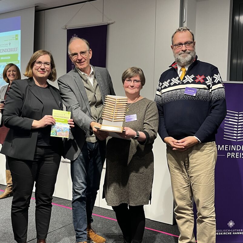 Eine Gruppe von Menschen halten ihren Preis auf der Bühne gemeinsam in Händen. 