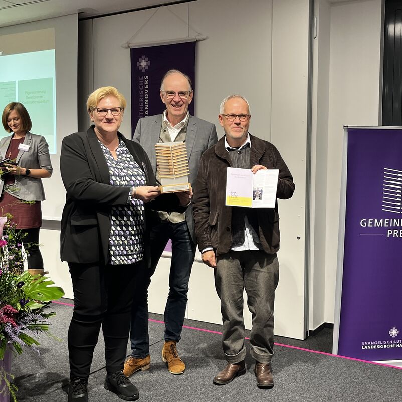 Eine Gruppe von Menschen halten ihren Preis auf der Bühne gemeinsam in Händen. 