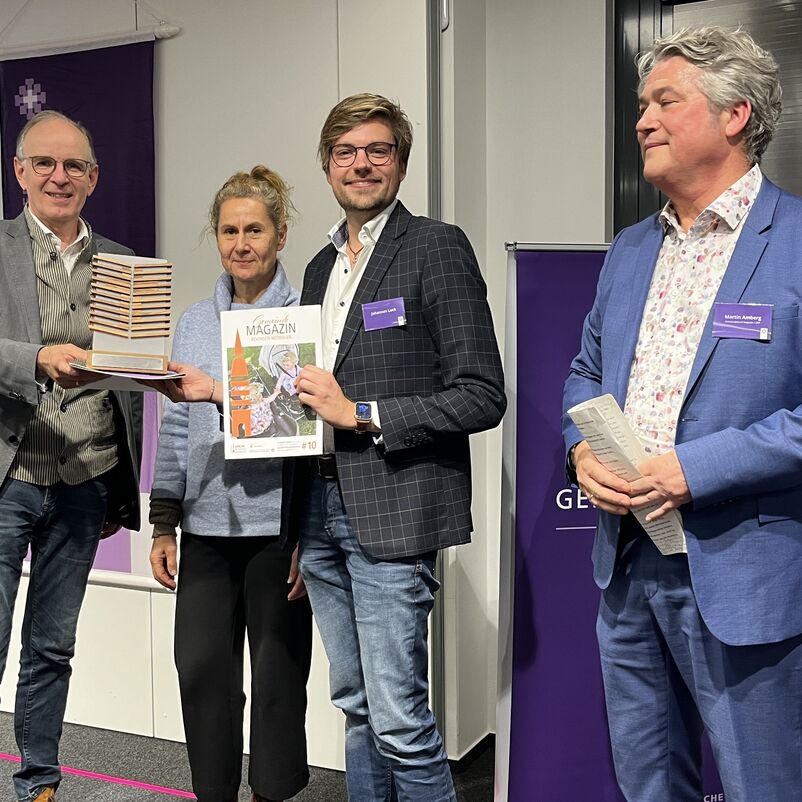 Eine Gruppe von Menschen halten ihren Preis auf der Bühne gemeinsam in Händen. 