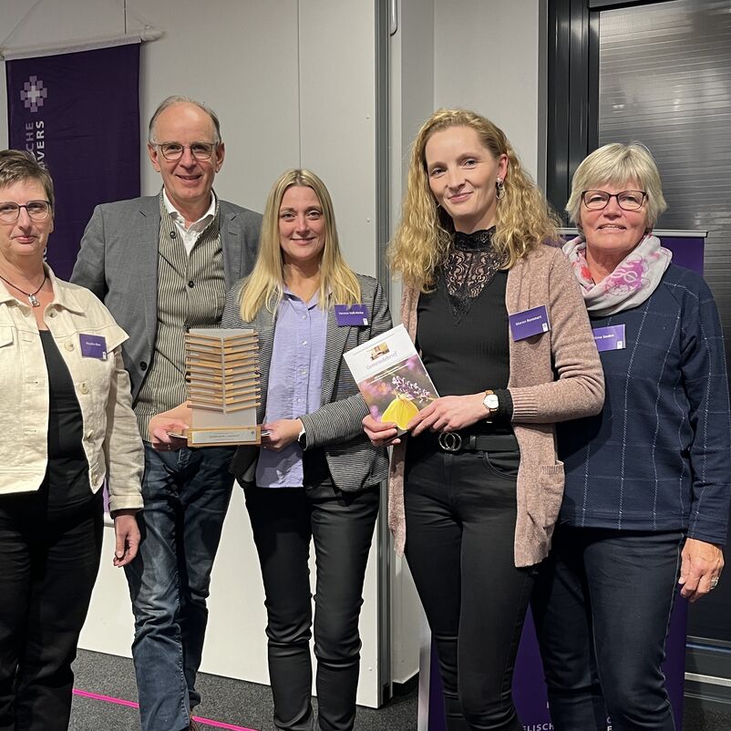 Eine Gruppe von Menschen halten ihren Preis auf der Bühne gemeinsam in Händen. 