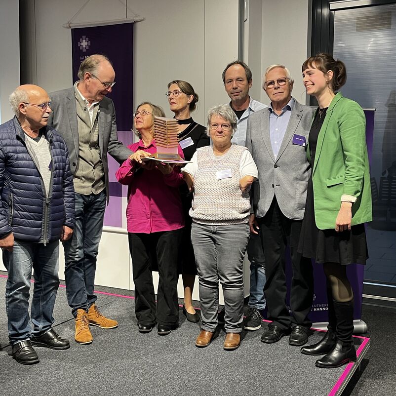 Eine Gruppe von Menschen halten ihren Preis auf der Bühne gemeinsam in Händen. 