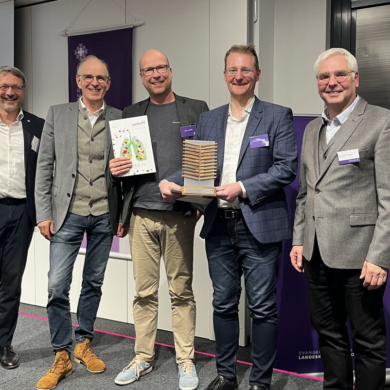 Eine Gruppe von Menschen halten ihren Preis auf der Bühne gemeinsam in Händen. 