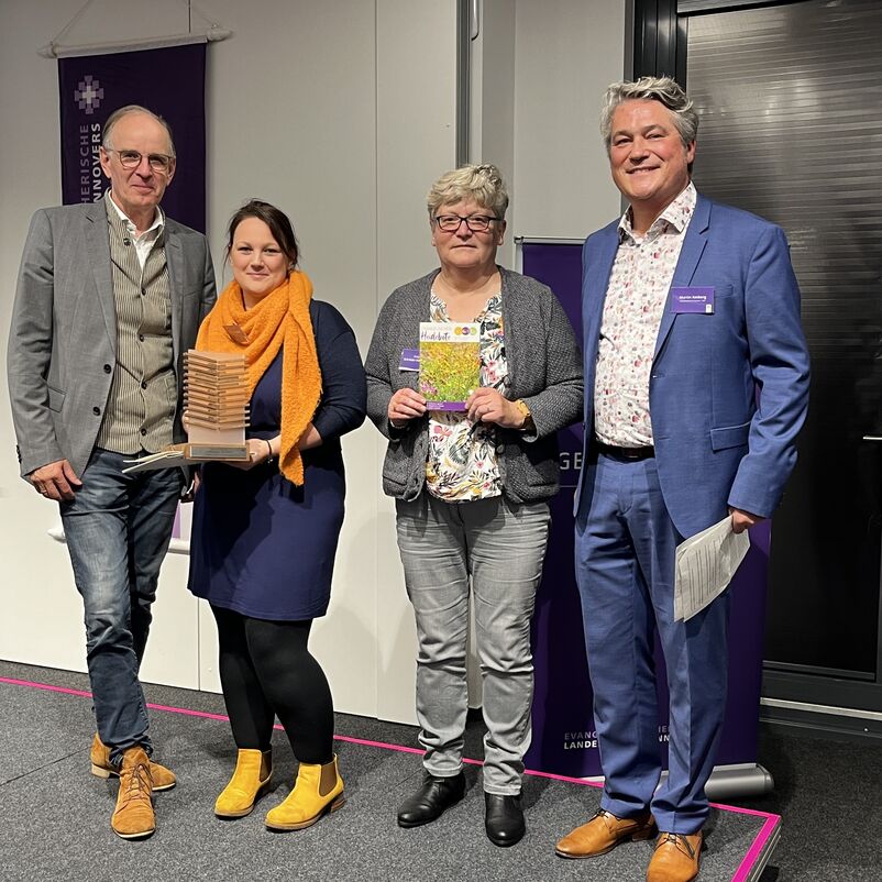 Eine Gruppe von Menschen halten ihren Preis auf der Bühne gemeinsam in Händen. 