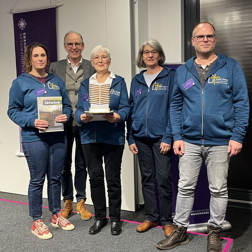 Eine Gruppe von Menschen halten ihren Preis auf der Bühne gemeinsam in Händen. 