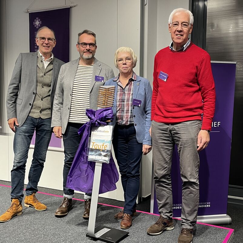 Eine Gruppe von Menschen halten ihren Preis auf der Bühne gemeinsam in Händen. 