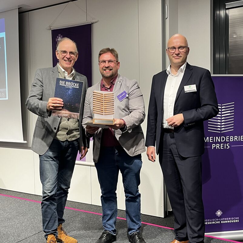 Eine Gruppe von Menschen halten ihren Preis auf der Bühne gemeinsam in Händen. 