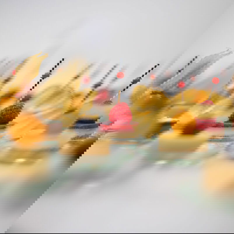 Auf einem Tisch stehen kleine Häppchen serviert. Im Fokus liegt ein Himbeer-Nachtisch.