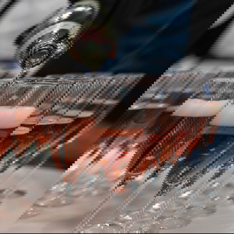 Auf einem Tisch stehen Sektgläser, die befüllt werden.