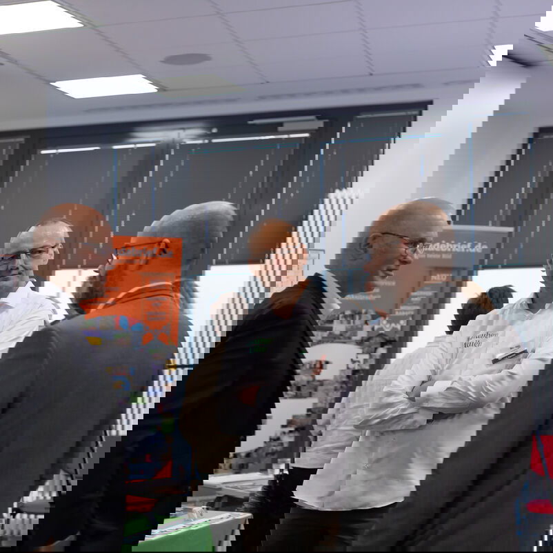 Drei männlich zu lesende Personen stehen im Kreis und unterhalten sich.