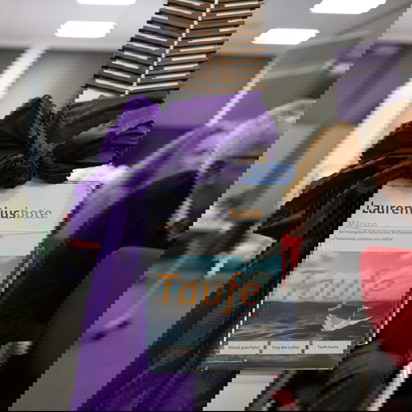 Ein Zeitschriftenhalter präsentiert den erstplatzierten Gemeindebrief. Eine lila Schleife umfasst die Halterung. Über der Haltung ist der Gemeindebriefpreis-Pokal installiert.