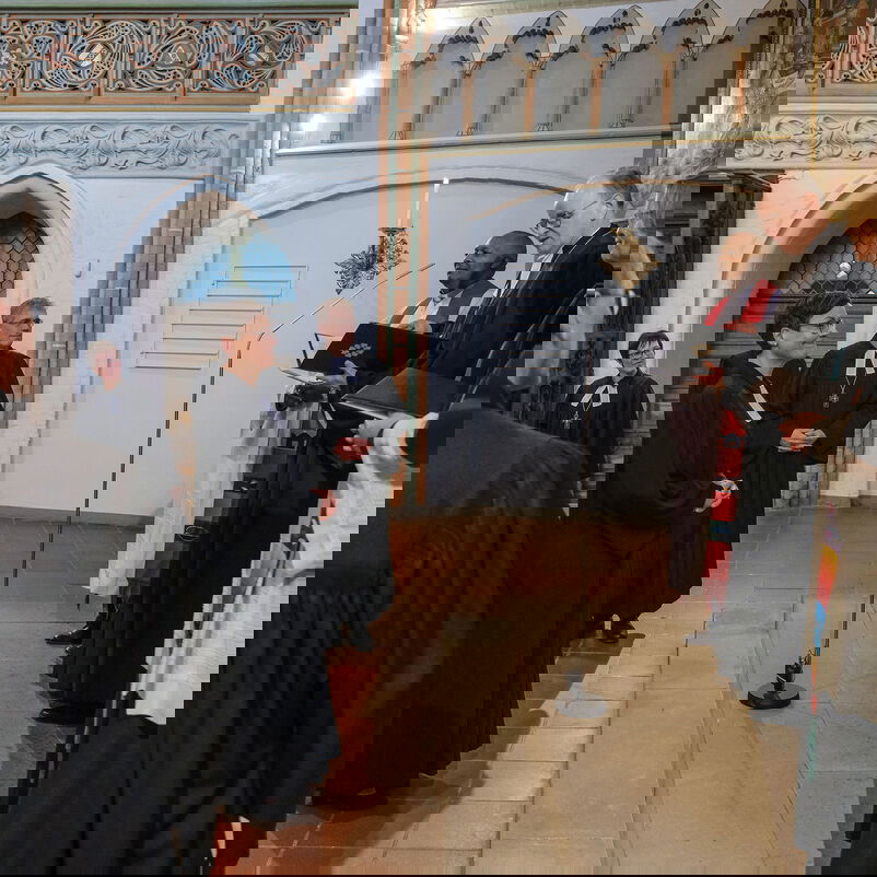 Ein weiblich zu lesende Person im Talar steht vor dem Altar. Auf der Altarstufe stehen mehrere männlich zu lesende Personen in geistlichen Gewändern.