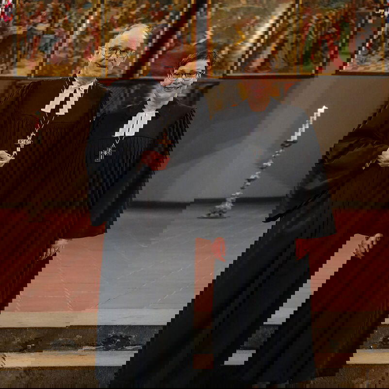 Eine männlich und eine weiblich zu lesende Person im Talar stehen vor einem Altar.