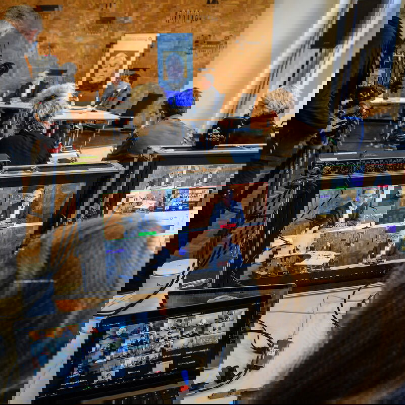 Ein Konferenzraum mit vielen Tischen, Kamerateams, Computerbildschirmen und Personen von hinten.