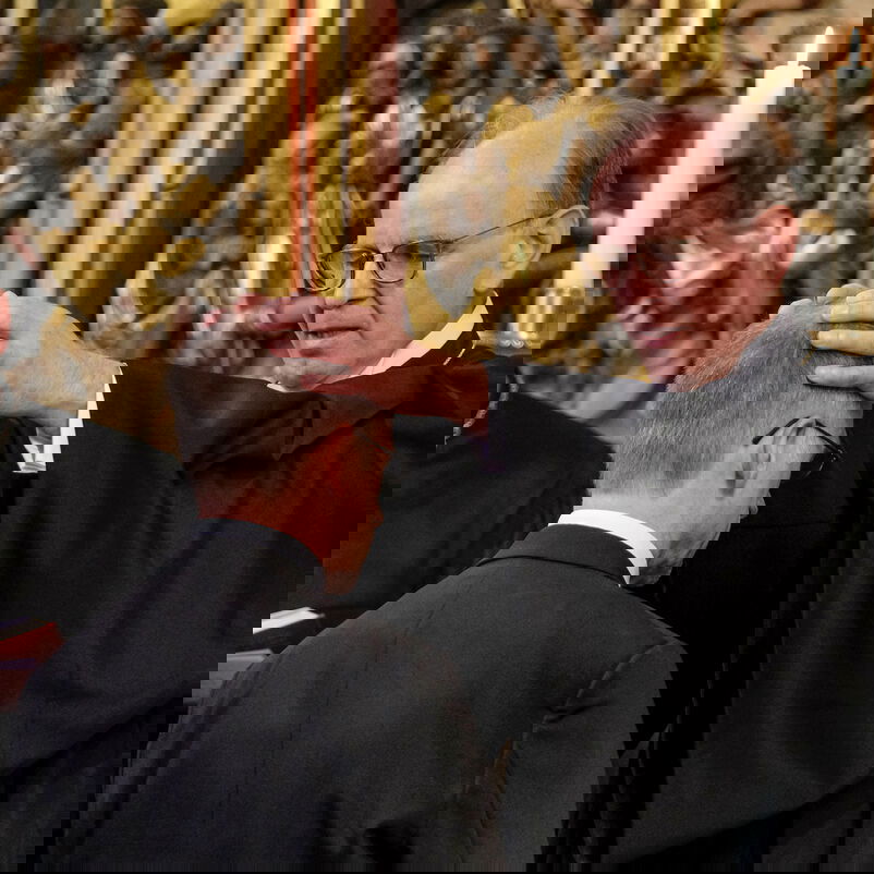 Eine männlich zu lesende Person im Altar segnet eine andere männlich zu lesende Person, in dem sie ihr die Hände auflegt.