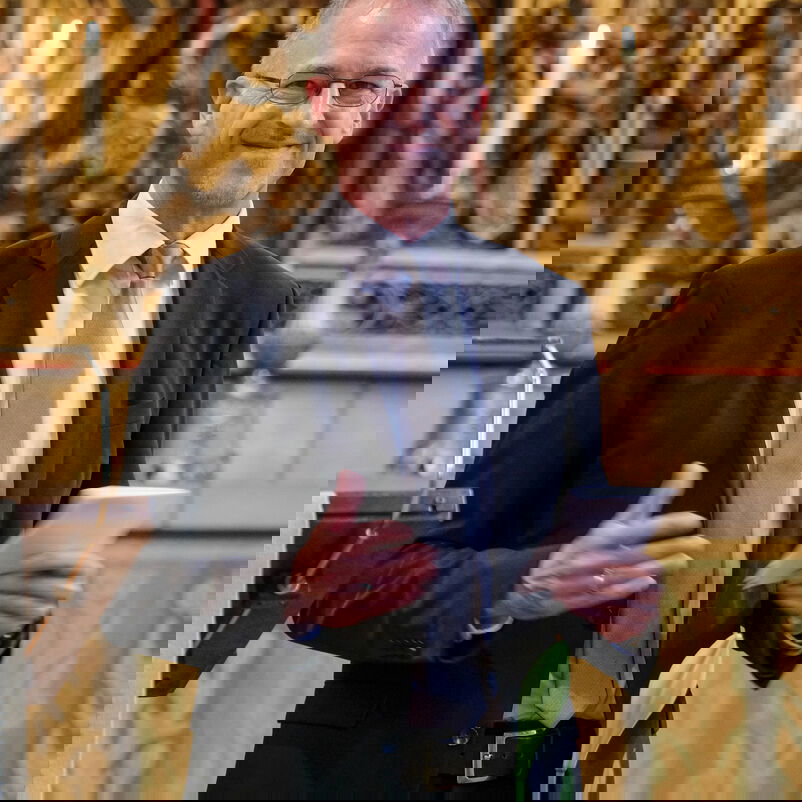 Eine männlich zu lesende Person steht vor einem goldenen Altarbild.