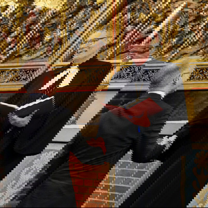 Eine männlich zu lesende Person im Talar schüttelt einer anderen männlich zu lesenden Person im Anzug die Hand.