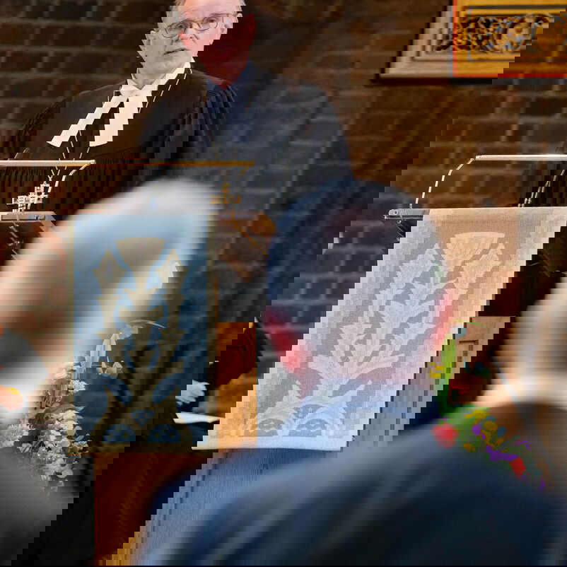 Eine männlich zu lesende Person im Talar spricht hinter einem Redepult in einer Kirche.