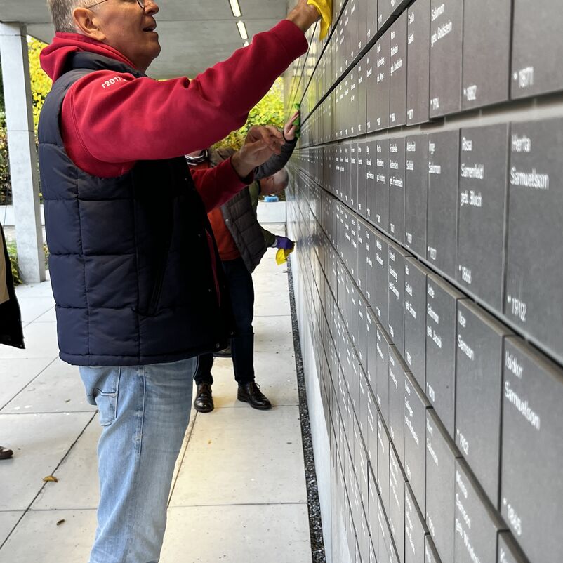 Eine männlich gelesene Person reinigt eine Namenstafel mit einem Wischlappen.