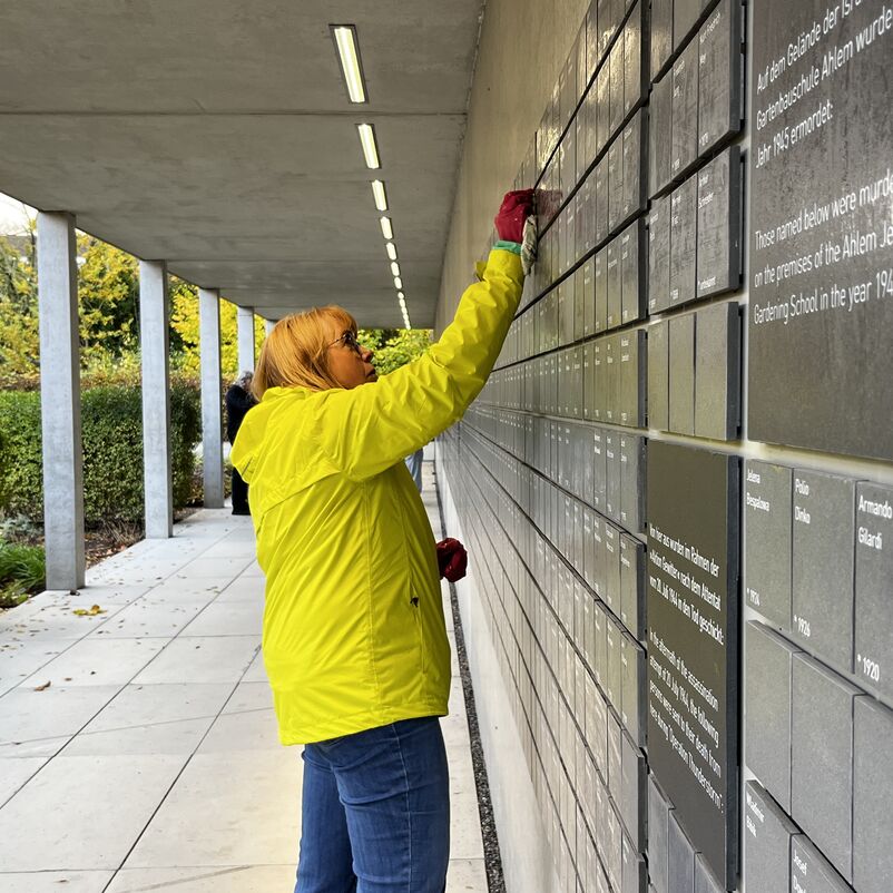 Einen weiblich gelesene Person putzt mit einem Wischlappen eine Namenstafel. 