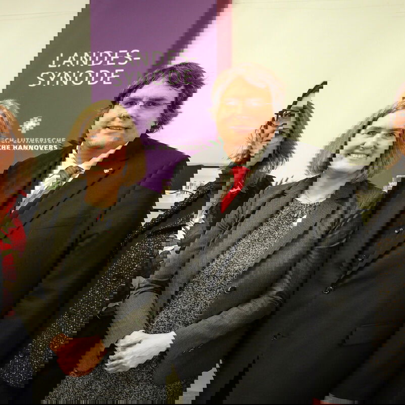 Drei weiblich und eine männlich zu lesende Person stehen nebeneinander und lächeln in die Kamera.