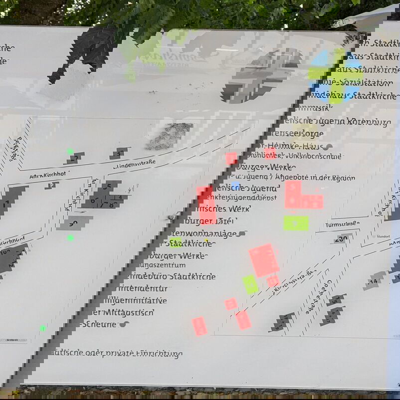 Fotografiert ist ein Schild, auf dem Grundstücke markiert sind, die um einen Kirchplatz liegen. 