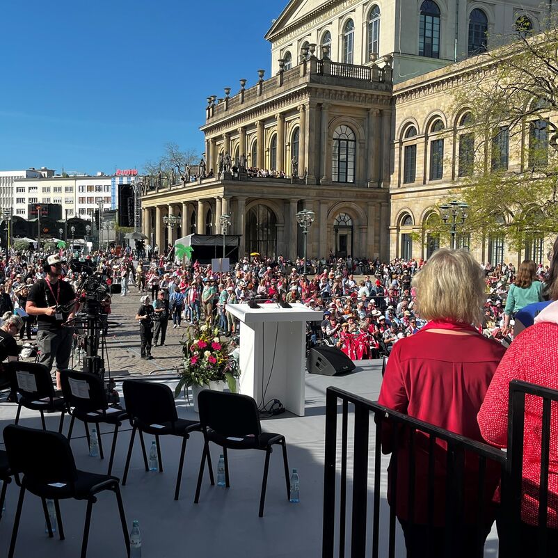 Blick von einer Bühne auf Menschen, die auf einem Platz sitzen.