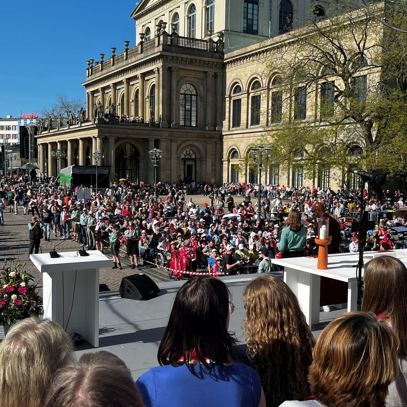 Menschen sitzen in vielen Stuhlreihen auf einem Platz.
