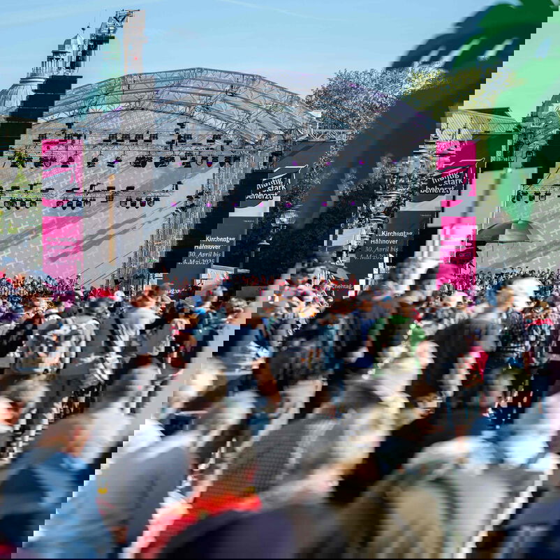 Blick über sitzende und stehende Menschen hinweg auf eine Bühne.