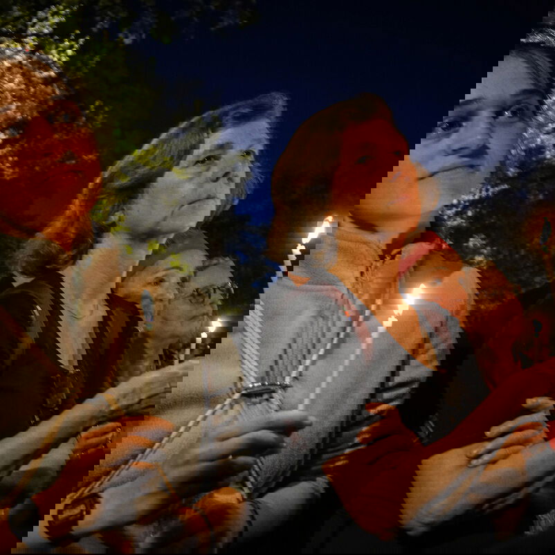 Zwei weiblich zu lesende Personen halten in der Dunkelheit Kerzen.