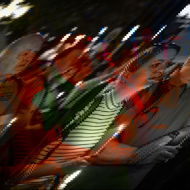 Weiblich und männlich zu lesende Personen halten in der Dunkelheit Kerzen.