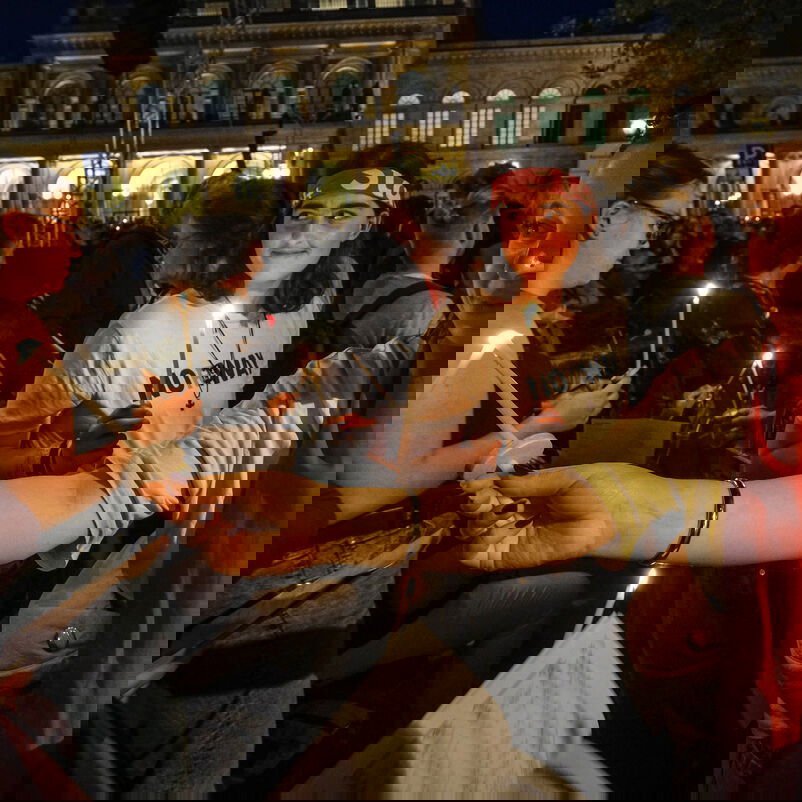 Weiblich und männlich zu lesende Personen geben untereinander Kerzenlicht weiter.