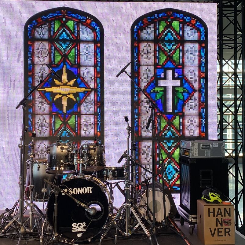Vor zwei bunten Kirchenfenstern steht ein Schlagzeug.