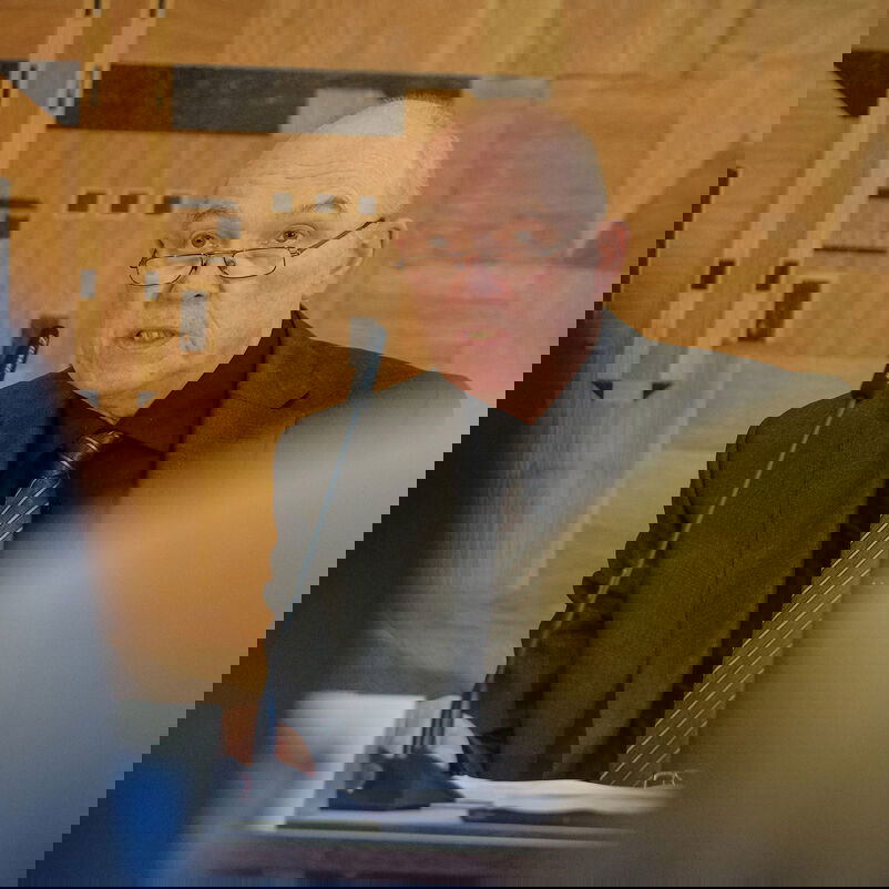 Eine männlich gelesene Person sitzt an einem Tisch.