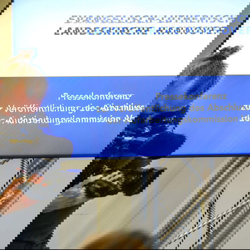 Eine männlich gelesene Person steht hinter einer Fernsehkamera.