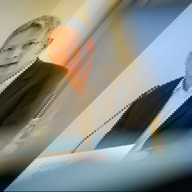 Eine männlich gelesene Person spricht an einem Mikrophon.