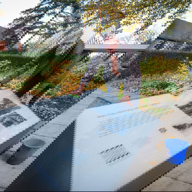 Eine männlich zu lesende Person reinigt eine Gedenktafel.