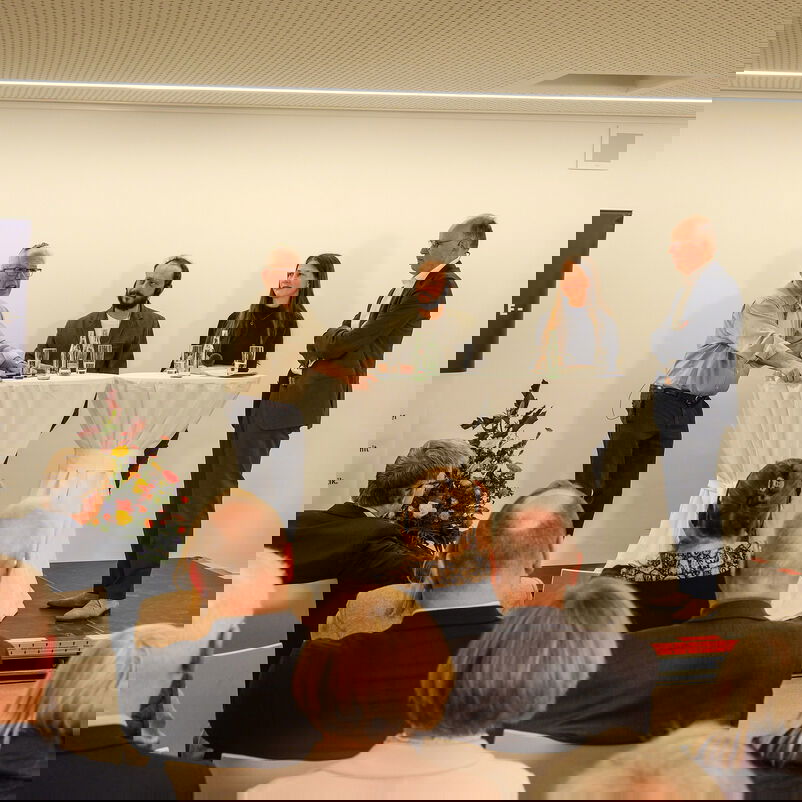 Drei männlich und eine weiblich zu lesende Person stehen an Stehtischen auf einem Podium und diskutieren.